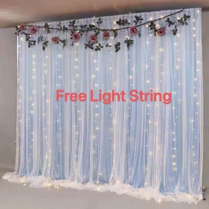 Peut inclure: Fond de scène en voile blanc avec une guirlande de fleurs roses et de verdure. Le texte "Free Light String" est écrit en rouge sur le rideau.