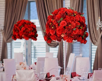 Könnte beinhalten: Zwei hohe weiße Vasen mit roten Rosensträußen als Mittelstücke für einen Hochzeitsempfang. Die Vasen stehen auf weißen Tischdecken mit weißen Stühlen und roten Servietten.