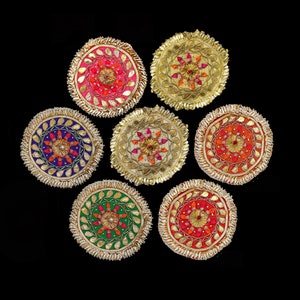May include: Seven round decorative embellishments with intricate designs. Each embellishment features a central floral motif surrounded by smaller floral patterns. The embellishments are in various colors, including pink, red, orange, green, blue, and gold.