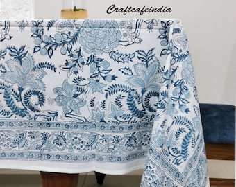 Puede incluir: Mantel blanco con un estampado floral azul. El mantel tiene un borde con un diseño floral repetido. El texto "craftcafeindia" es visible en el mantel. Una copa de líquido con una rodaja de lima está sobre la mesa.