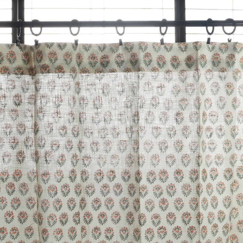 May include: White sheer curtains with a delicate floral pattern in shades of pink and green. The curtains are hung on a black rod with silver hooks.