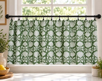 May include: A cafe curtain featuring a repeating white floral and botanical pattern on a dark green background, suspended from a black metal rod with matching black rings. The fabric hangs in soft, vertical folds across the window frame.