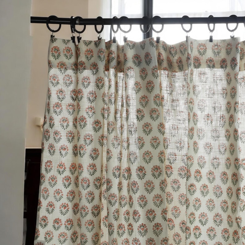 May include: White sheer curtains with a floral pattern in shades of pink and green. The curtains are hung on a black curtain rod.