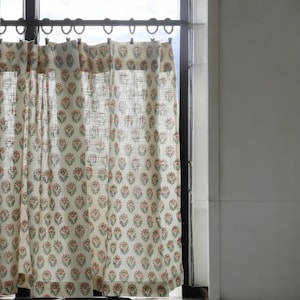 May include: A pair of white sheer curtains with a floral pattern in shades of pink and green. The curtains are hung on a metal rod with hooks.