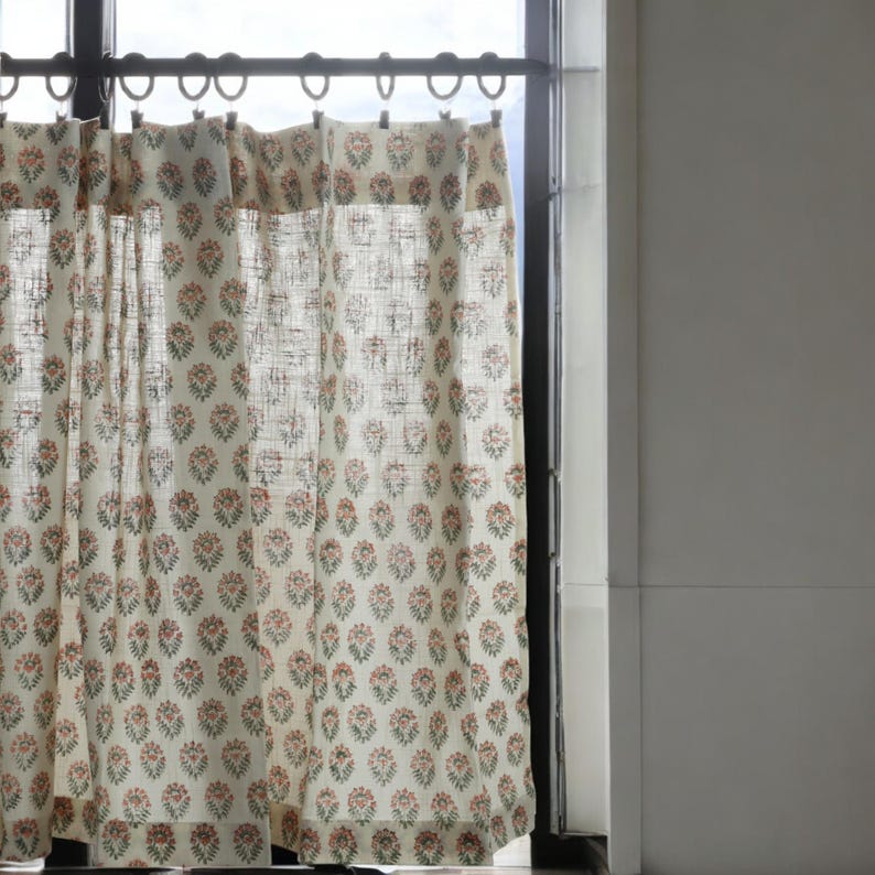 May include: A pair of white sheer curtains with a floral pattern in shades of pink and green. The curtains are hung on a metal rod with hooks.