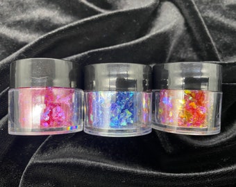 May include: Three small jars of iridescent glitter, one pink, one blue, and one orange.