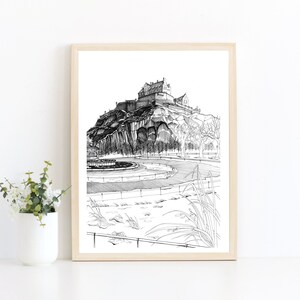 K&ouml;nnte beinhalten: Schwarz-Wei&szlig;-Zeichnung eines Schlosses auf einem H&uuml;gel, gerahmt in hellem Holz. Das Kunstwerk zeigt das Schloss, B&auml;ume und einen Brunnen im Vordergrund. Der Stil ist detailliert und illustrativ.