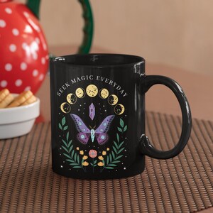 May include: Black ceramic mug with a white design featuring a butterfly, moon phases, and the text "Seek Magic Everyday".