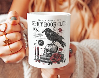 May include: White ceramic mug with a black raven, skull, and roses design. The mug reads "Proud Member of the Spicy Book Club".