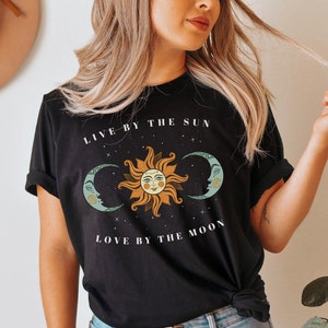 May include: Black t-shirt with a graphic of a sun and two moons with the text "Live by the sun, love by the moon".