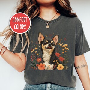K&ouml;nnte beinhalten: Ein anthrazitfarbenes T-Shirt mit einem floralen Design, das einen Chihuahua zeigt. Der Text "Comfort Colors" befindet sich auf einem roten Kreis in der oberen linken Ecke des Bildes. Das Model tr&auml;gt Gr&ouml;&szlig;e M in der Farbe "Pepper".