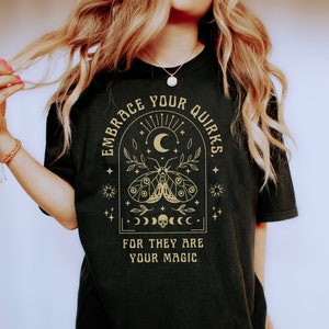 May include: Black t-shirt with a gold graphic design featuring a moth, crescent moon, stars, and the text "Embrace Your Quirks. For They Are Your Magic."