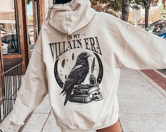 May include: A cream-colored hoodie with a black raven graphic and the text "In My Villain Era" printed on the back.