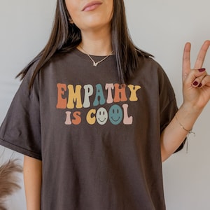 May include: A brown t-shirt with the text "EMPATHY IS COOL" in colorful letters with smiley faces.