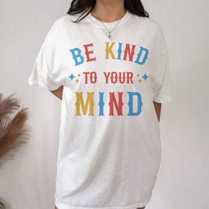 May include: White oversized t-shirt with the text "BE KIND TO YOUR MIND" in colorful block letters.