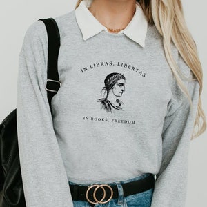 May include: Grey sweatshirt with a black and white illustration of a woman's face and the text "In Libras, Libertas. In Books, Freedom."