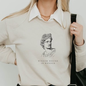 May include: A beige sweatshirt with a graphic of a man's face and the text "Wisdom begins in wonder".