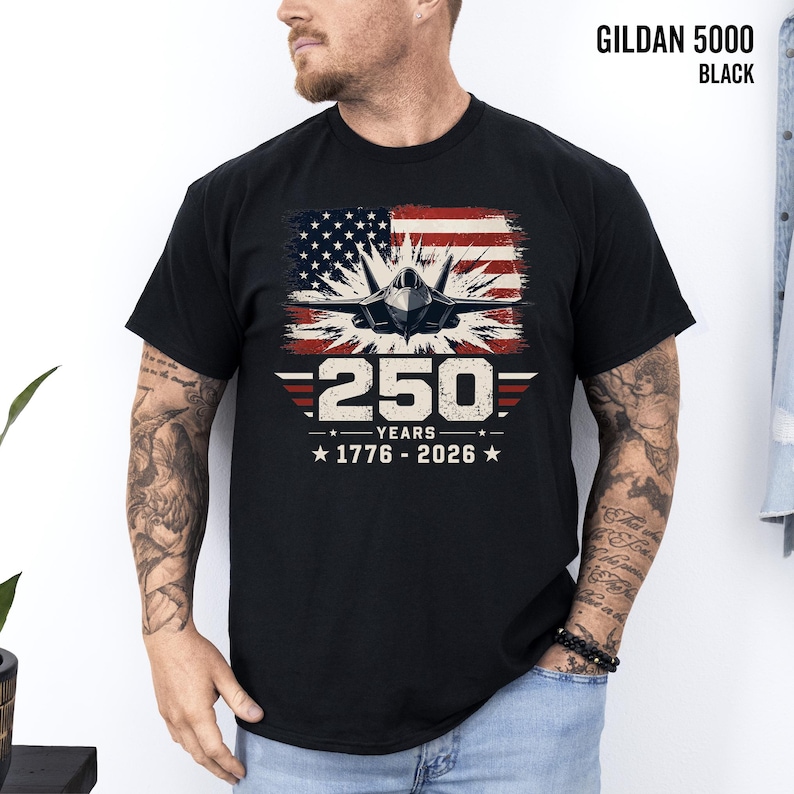 May include: Black t-shirt with a graphic featuring a fighter jet in front of a distressed American flag. The design includes the text "250 YEARS 1776-2026". The shirt is a Gildan 5000 in black.