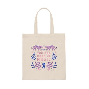 Op de afbeelding: Cr&egrave;mekleurige draagtas met een ontwerp met twee roze en paarse tijgers die tegenover elkaar staan, met de tekst "YOU ARE MADE OF MAGIC". Het ontwerp bevat ook blauwe bladeren, slangen en sterren.