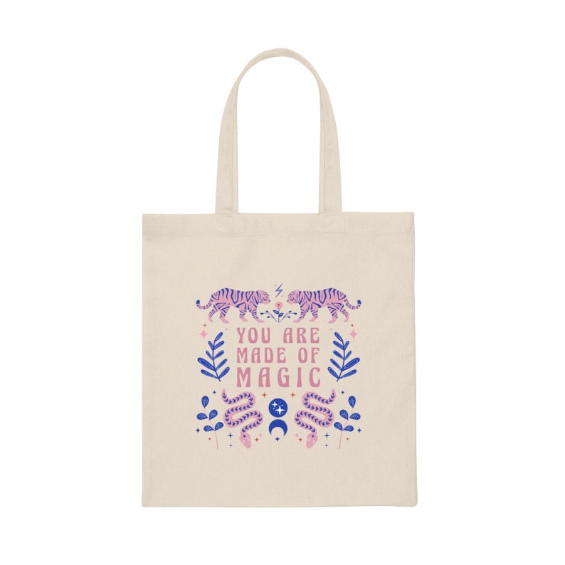 Op de afbeelding: Cr&egrave;mekleurige draagtas met een ontwerp met twee roze en paarse tijgers die tegenover elkaar staan, met de tekst "YOU ARE MADE OF MAGIC". Het ontwerp bevat ook blauwe bladeren, slangen en sterren.