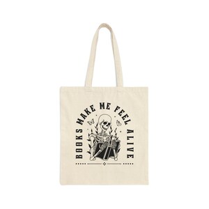 Pu&ograve; includere: Una borsa di tela beige con testo nero e un'immagine di uno scheletro che legge un libro. Il testo dice "I libri mi fanno sentire vivo".