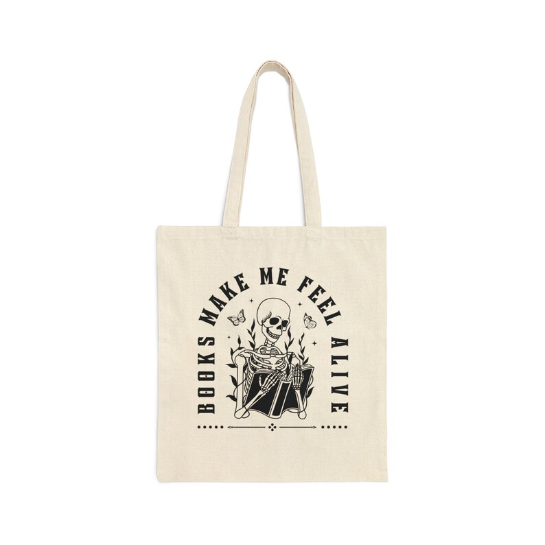 Pu&ograve; includere: Una borsa di tela beige con testo nero e un'immagine di uno scheletro che legge un libro. Il testo dice "I libri mi fanno sentire vivo".