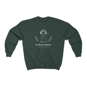 May include: A dark green sweatshirt with a white graphic of a bust of a woman with a laurel wreath around her head. The text "In Libras, Libertas" is below the image, and the text "In books, freedom" is below that.