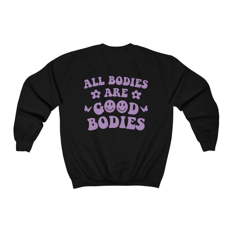 May include: Black sweatshirt featuring the lavender text "ALL BODIES ARE GOOD BODIES". The design incorporates flowers, smiley faces, and butterflies. A relaxed, casual top for everyday wear.