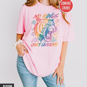 May include: A light pink t-shirt with the text "NO KINGS ONLY QUEENS" and a colorful tiger graphic. The shirt is labeled "Comfort Colors" and "Blossom".