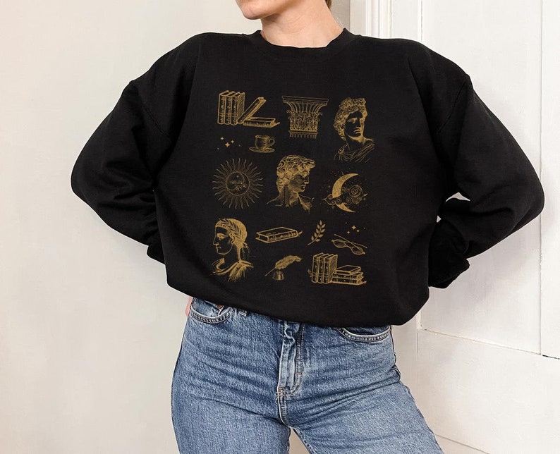 Puede incluir: Sudadera negra con un estampado gr&aacute;fico dorado de varias ilustraciones, incluyendo libros, una taza, un sol, una luna y un busto de una persona.