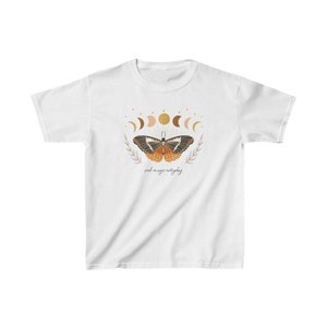 Peut inclure: T-shirt blanc avec un motif de papillon aux ailes orange et noires, entour&eacute; d'un croissant de lune et d'&eacute;toiles. Le texte "seek magic everyday" est imprim&eacute; sous le papillon.