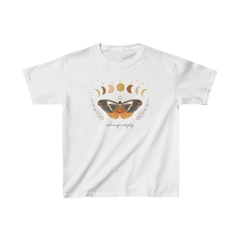 Peut inclure: T-shirt blanc avec un motif de papillon aux ailes orange et noires, entour&eacute; d'un croissant de lune et d'&eacute;toiles. Le texte "seek magic everyday" est imprim&eacute; sous le papillon.