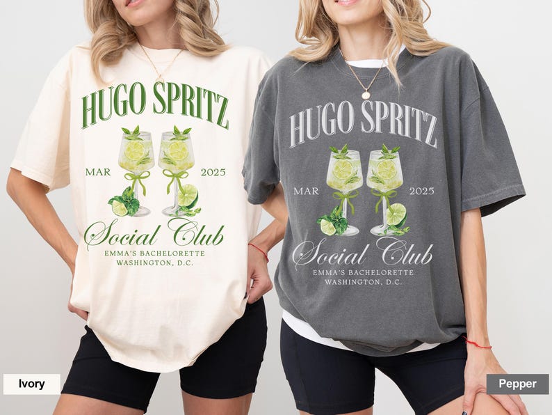 May include: Two white and gray t-shirts with a graphic design of two glasses of Hugo Spritz, a cocktail, with the text "Hugo Spritz" and "Social Club" on the front. The text "MAR 2025" is also on the front of the shirts. The shirts are on two models wearing black shorts.