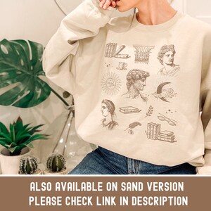 Puede incluir: Una sudadera beige con un estampado gr&aacute;fico de varias ilustraciones, incluyendo libros, un sol, una luna, un busto de un hombre y una persona con una corona. El texto "ALSO AVAILABLE ON SAND VERSION PLEASE CHECK LINK IN DESCRIPTION" est&aacute; impreso en la parte inferior de la sudadera.