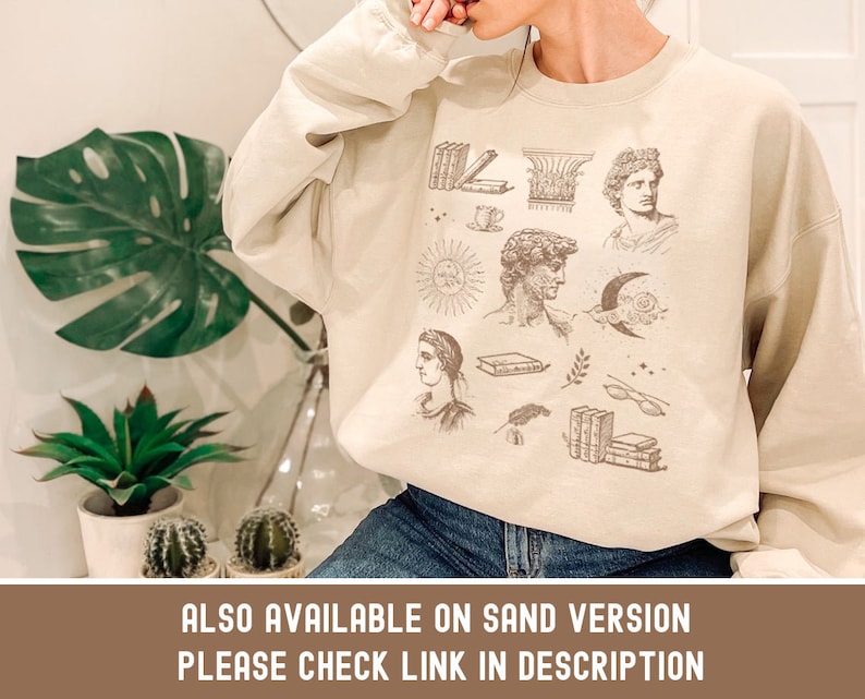 Puede incluir: Una sudadera beige con un estampado gr&aacute;fico de varias ilustraciones, incluyendo libros, un sol, una luna, un busto de un hombre y una persona con una corona. El texto "ALSO AVAILABLE ON SAND VERSION PLEASE CHECK LINK IN DESCRIPTION" est&aacute; impreso en la parte inferior de la sudadera.