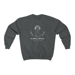 May include: A dark heather grey sweatshirt with a white graphic design featuring a bust of a woman with laurel branches and the text "In Libras, Libertas" and "In books, freedom".