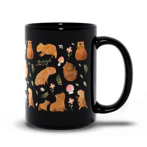 May include: Black ceramic coffee mug with a white design of capybaras, mushrooms, and flowers.