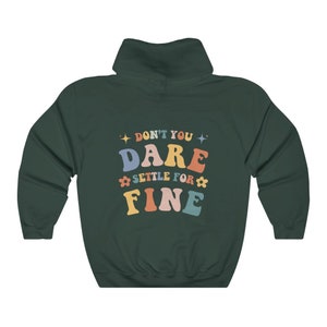 Puede incluir: Una sudadera con capucha verde oscuro con el texto "Don't you dare settle for fine" en letras retro de colores.