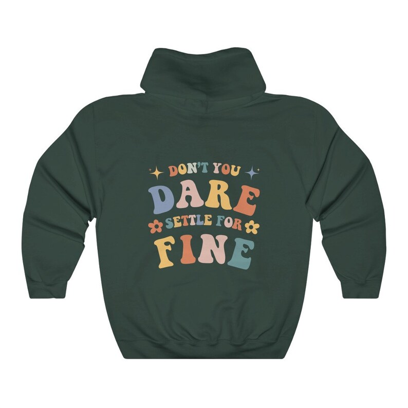 Puede incluir: Una sudadera con capucha verde oscuro con el texto "Don't you dare settle for fine" en letras retro de colores.