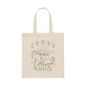 K&ouml;nnte beinhalten: Eine beige Tragetasche mit einer schwarz-wei&szlig;en Illustration von Pilzen und einem Halbmond-Design. Die Tasche hat einen schwarzen Griff.