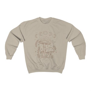 May include: A beige sweatshirt featuring a line drawing of mushrooms and a crescent moon design. The design is in a brown colour.