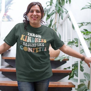 May include: A dark green t-shirt with the text "Throw Kindness Around Like Confetti" in colourful retro lettering. A smiley face is included in the text.
