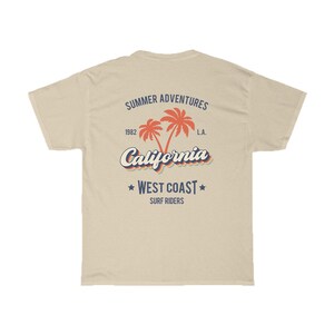 May include: A beige t-shirt with a vintage-style graphic design featuring palm trees, the text "Summer Adventures", "1982", "L.A.", "California", "West Coast", and "Surf Riders".