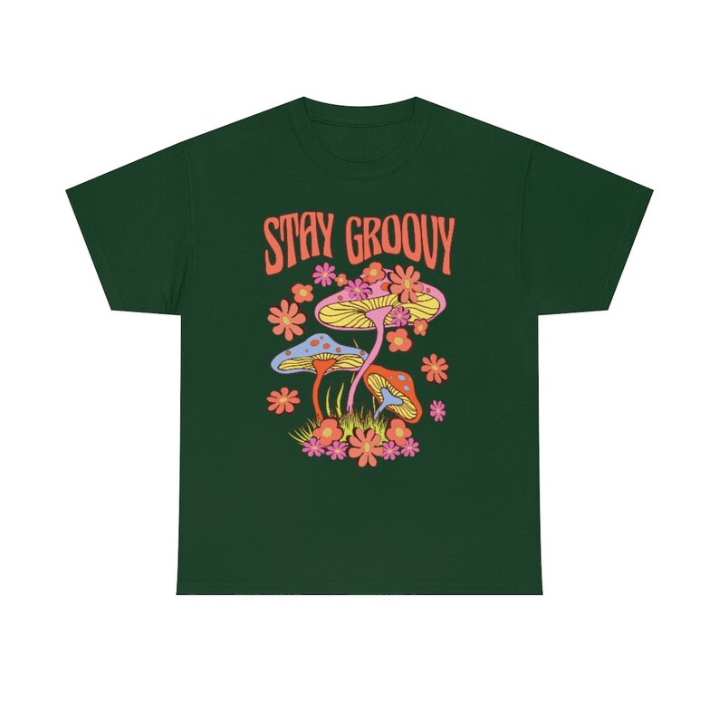 May include: Dark green t-shirt featuring a colorful graphic of mushrooms and flowers. The text "STAY GROOVY" is printed in orange above the illustration. The design includes yellow, pink, orange, and blue elements, creating a vibrant and retro aesthetic.