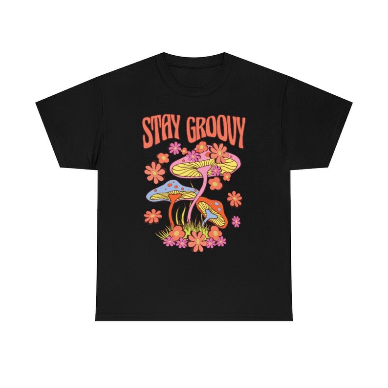 May include: Black t-shirt with a colorful graphic of mushrooms and flowers. The text "STAY GROOVY" is in orange above the illustration. The design features blue, yellow, orange, and pink elements, creating a vibrant and retro aesthetic.