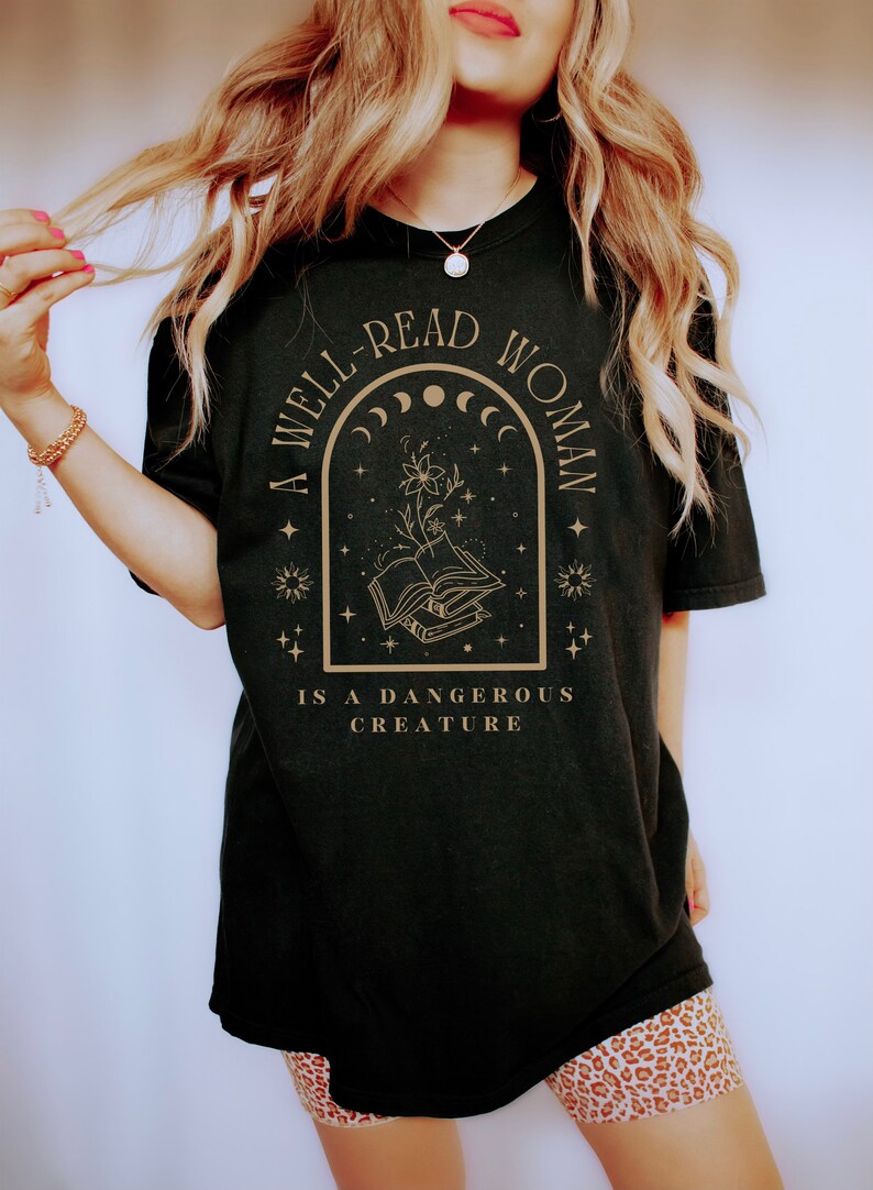 May include: A black t-shirt with a gold graphic design that reads "A well-read woman is a dangerous creature". The graphic features a book, a flower, and stars.