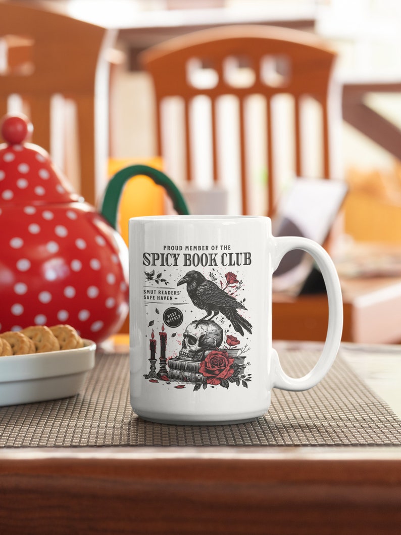 Puede incluir: Taza de cer&aacute;mica blanca con una ilustraci&oacute;n en blanco y negro de un cuervo posado sobre una calavera con una rosa roja. El texto "Proud Member of the Spicy Book Club" est&aacute; impreso en la taza. El texto "Smut Readers' Safe Haven" tambi&eacute;n est&aacute; impreso en la taza.