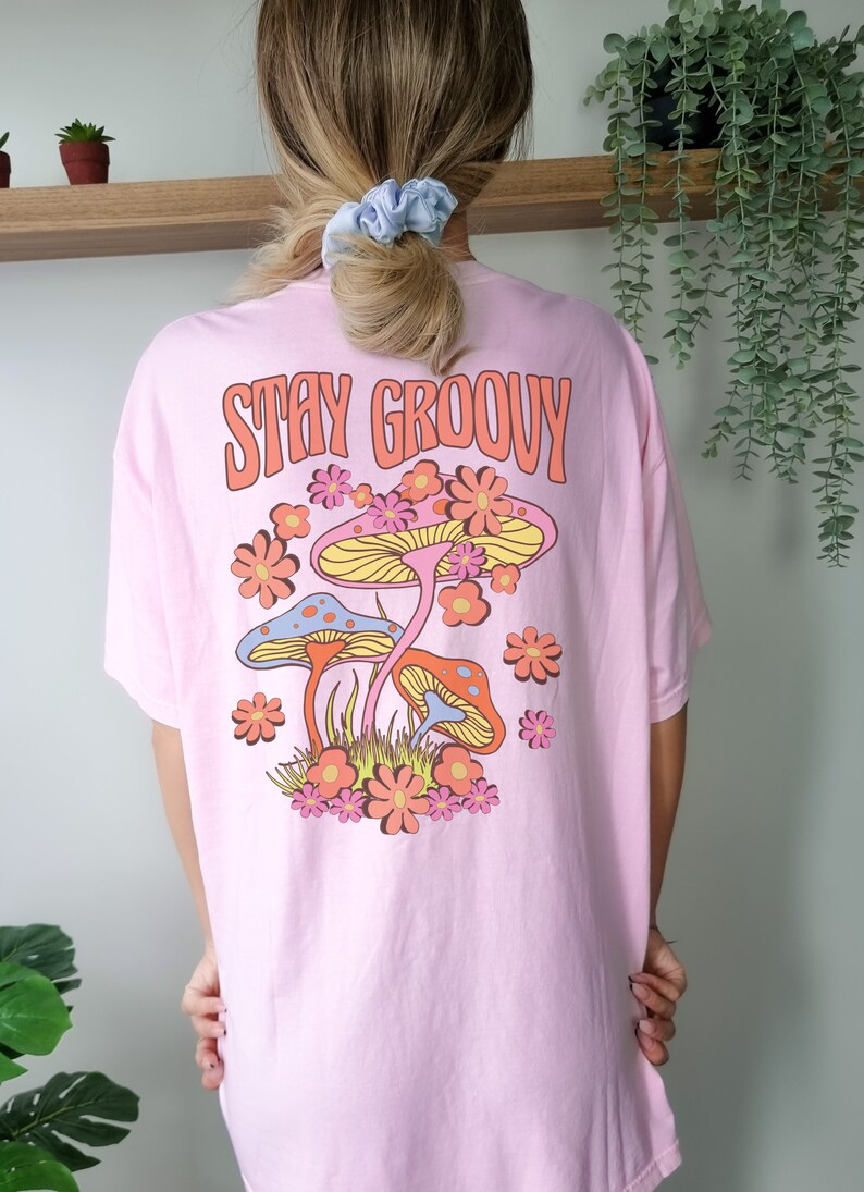 May include: Pink t-shirt with the text "Stay Groovy" and a retro graphic of mushrooms and flowers.