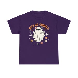 May include: Purple short-sleeved t-shirt with a white ghost wearing a flower crown and peace signs. The text "Let's Go Ghouls" is in orange and yellow letters.