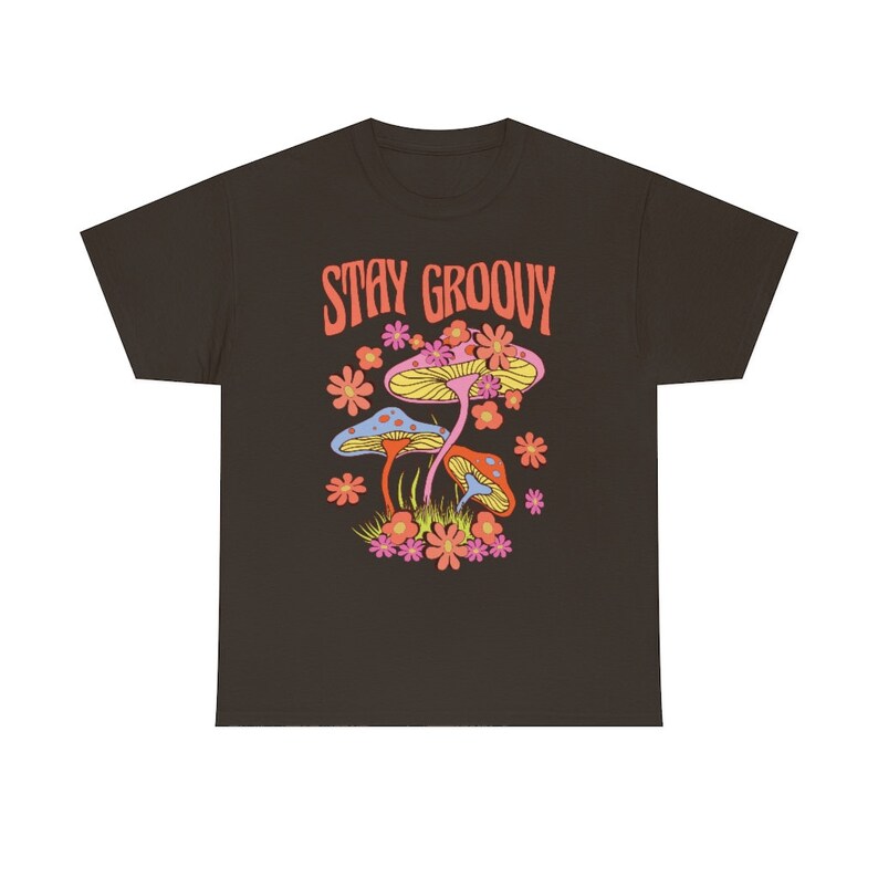 May include: A dark brown t-shirt featuring a colorful graphic of mushrooms and flowers. The text "STAY GROOVY" is printed above the illustration in orange. The design has a retro, psychedelic vibe.